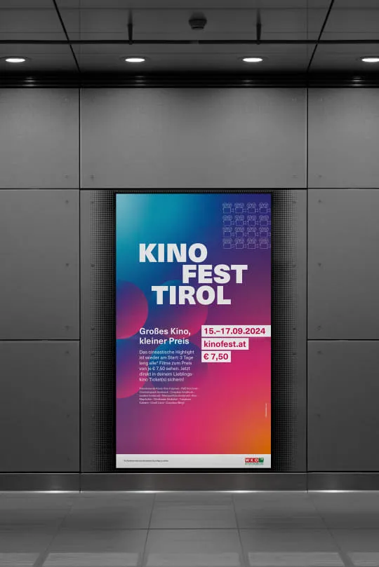 Auf einer Monitorwerbung in einer öffentlichen Begegnungszone wird das Sujet des Kinofest Tirol angezeigt. Das farbenfrohe Design reicht von Blau über Lila/Rosa bis Gelb und präsentiert in weißer Schrift die wichtigsten Fakten zum Kinofest Tirol.