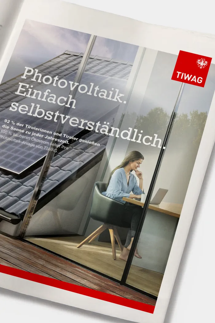 Eine ganzseitige Printanzeige zeigt eine Dame, die am Tisch sitzt und in ihren Laptop blickt. Im Hintergrund ist eine auf dem Dach montierte PV-Anlage sichtbar. Neben der Headline und dem Subtext der Kampagne ist das TIWAG-Logo abgebildet.