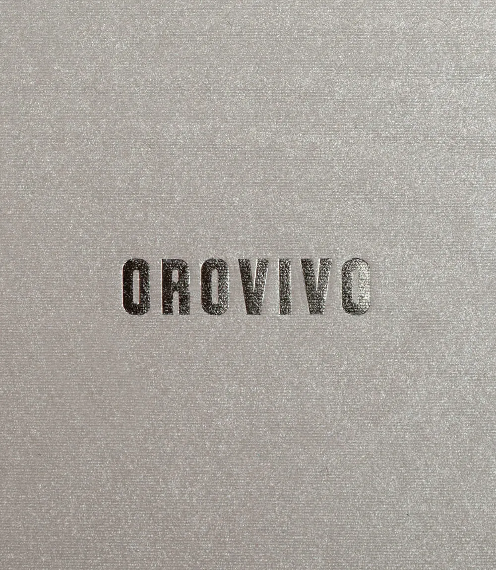 Schwarze Prägung des OROVIVO-Logos auf schimmernder, strukturiert-beiger Oberfläche.
